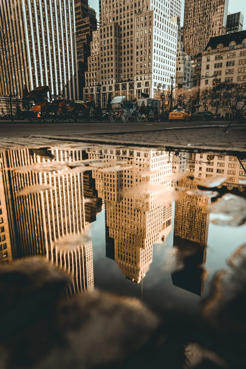 New York buildings and a yellow taxi reflected in a street puddle